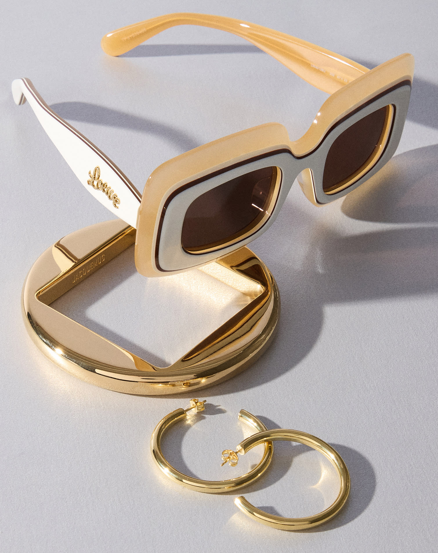 Bracciale rigido dorato, orecchini a cerchio dorati e occhiali da sole Loewe beige e bianchi