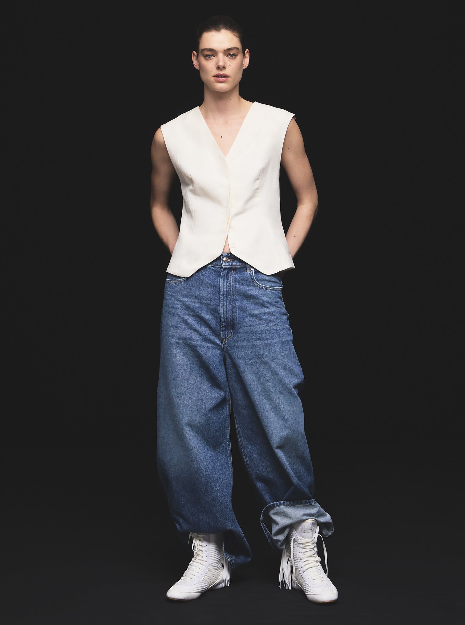 Femme vêtue d'un gilet blanc, d'un jean en denim et d'une paire de baskets.