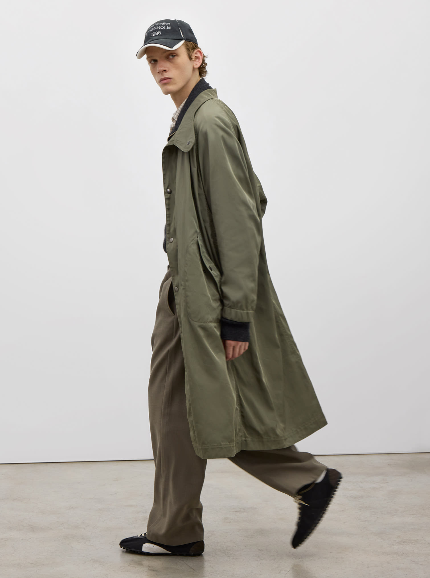 Men look with polyester green trench, green pants, baseball cap and black low sneakers