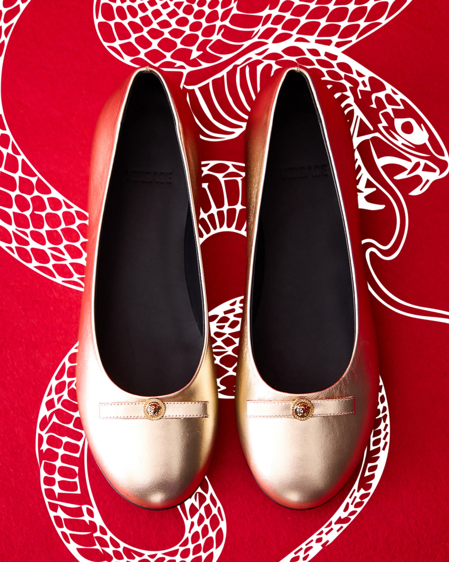 Ballerine Versace in pelle metallizzata con fiocco. Serpente bianco su sfondo rosso.