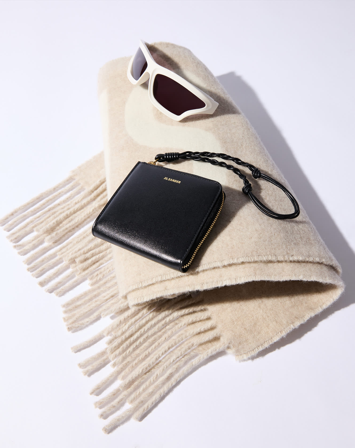 Sciarpa beige con frange, occhiali da sole bianchi e portafoglio in pelle nera con laccino