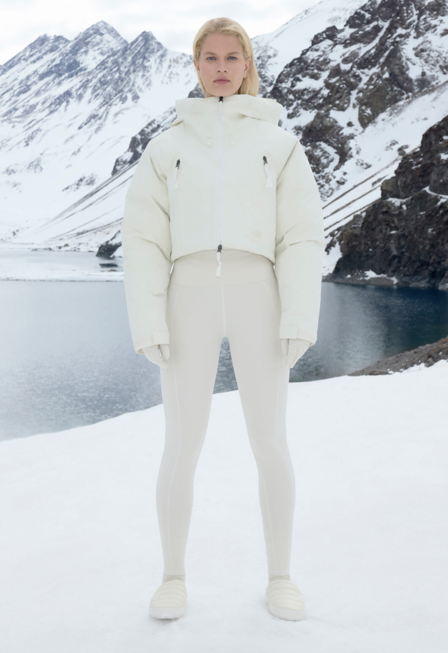 Modella in outfit da neve bianco The North Face x Skims in montagna con lago